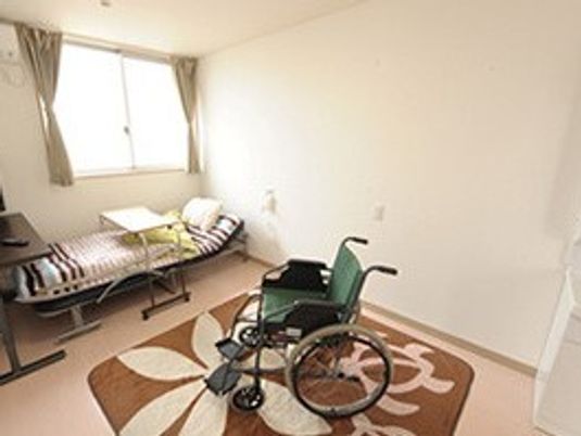 介護用ベッドや車いす、敷物がある施設内の居室の様子。一人用の部屋の写真