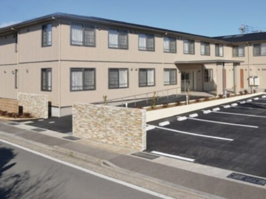 エル字型の２階建ての建物は日当たり良好で敷地内には駐車場があり、玄関先には手すり付きのスロープがある。