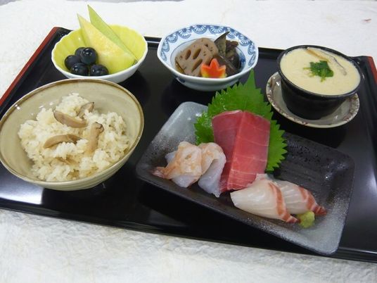 炊き込みご飯や刺身の盛り合わせ、煮物、フルーツの盛り合わせ、茶碗蒸しなどが並んでいる。