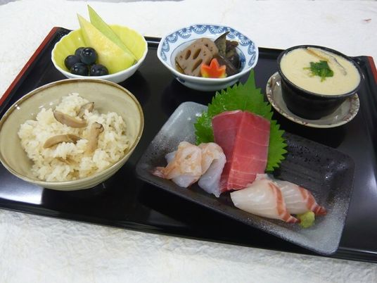 炊き込みご飯や刺身の盛り合わせ、煮物、フルーツの盛り合わせ、茶碗蒸しなどが並んでいる。