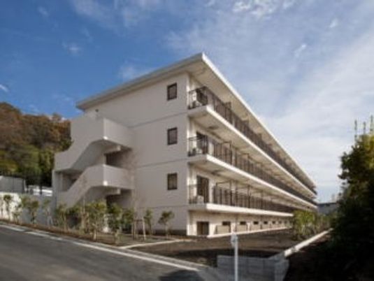 マンション風の建物が天気の良い日に撮影されている。周辺は自然豊かな場所