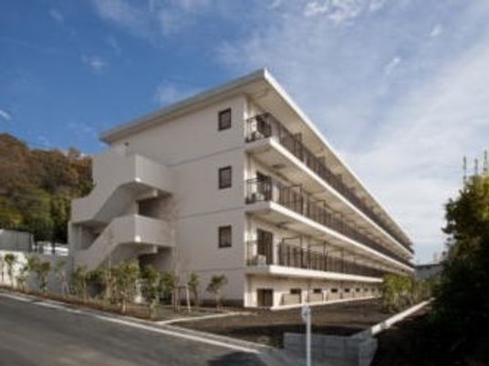マンション風の建物が天気の良い日に撮影されている。周辺は自然豊かな場所
