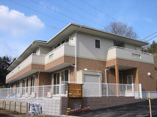 グループホームことりの森と書かれた手作りの看板。1階が茶色、2階が白い外壁になっている2階建て建築物