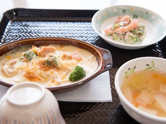 グラタンとおかず類が並んでいる洋食風メニュー。お盆の上に乗った高齢者向けの食事