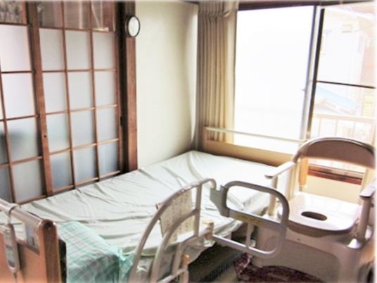 介護用ベッドが置いてある一軒家の一室。高齢者用の椅子がある小さな部屋