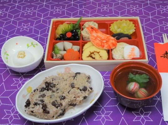 赤飯に吸い物、なますと6つの仕切りに分けられたお弁当風のおせち。寿と書かれた箸が添えられている。