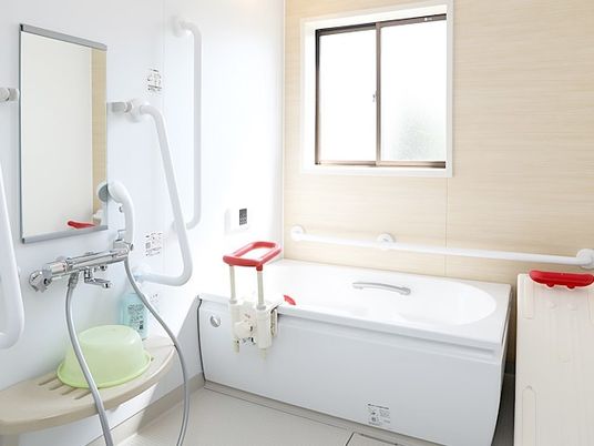 手すりが付いたシャワスペースと座った姿勢を楽にできる器具付きの浴槽の写真