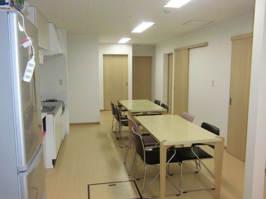 小さなテーブルが２つ並べられている施設のリビングスペース