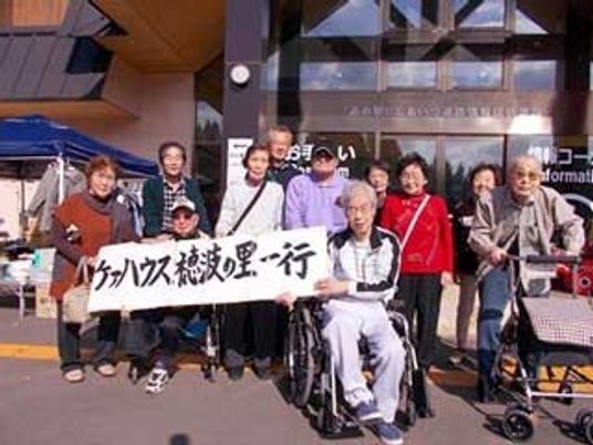 車いすを利用している人も参加している外出ベント。「ケアハウス稲波の里一行」と書かれた垂れ幕を持っている。
