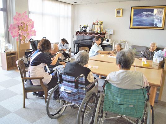 施設内の小さなリビングに集まって会話を交わすスタッフと高齢者の様子