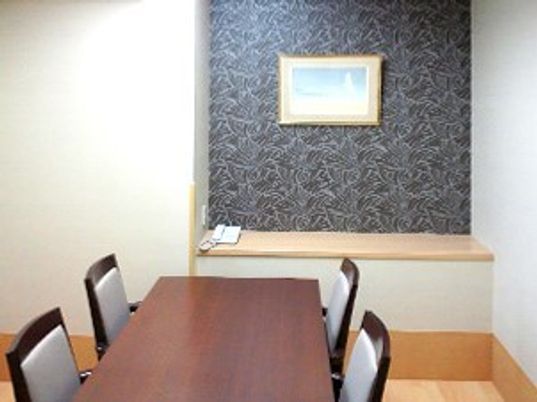 相談室には絵画や電話が置かれ、対面式に椅子が置かれたテーブルがある。