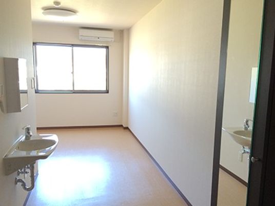部屋の入り口から奥のほうを写した写真。窓とエアコン、照明などが付いているワンルーム