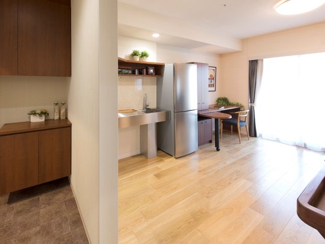 広めの部屋の玄関とキッチン部分が写っている。大きめの冷蔵庫がある 普通のお住まいと変わらない、上質な空間を目指しました。ご利用者様らしいお部屋に仕立てていただけます。