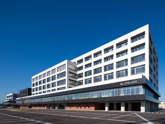 青空が広がっている写真。鉄骨造の背の高い建物。下に病院がある