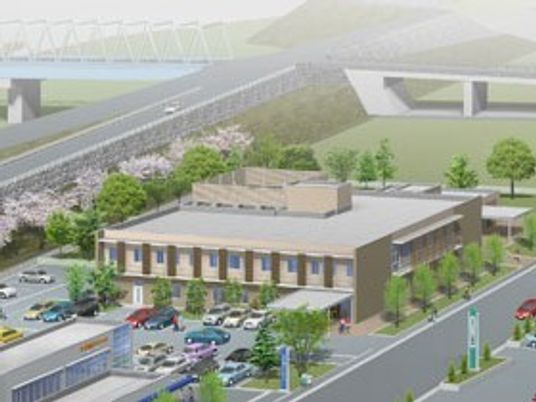 広い敷地にある２階建てのベージュの建物の周りには、駐車場や木が植えられ、桜並木もある。