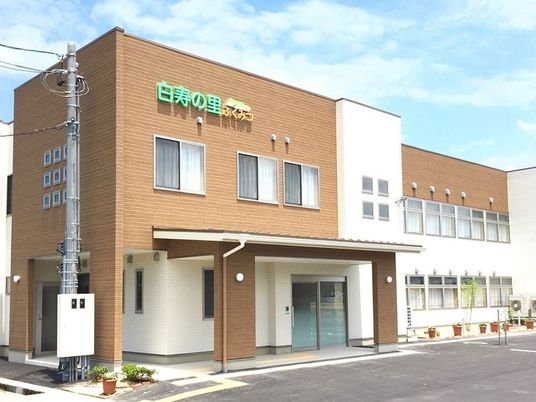 2階建ての建物。ブラウンと白のモダンなデザインでプランターには花も植えられている。