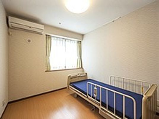 介護用ベッドが置かれたフローリングの居室には大きな窓とエアコンが付いている。