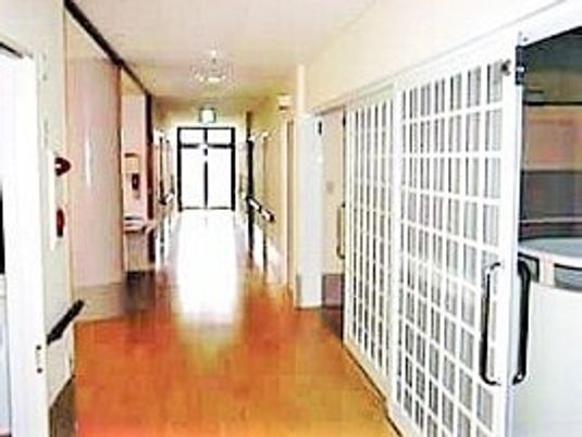 フローリング仕様の床と長く続く廊下が写っている。手すりが見えていて施設内の設備もある様子
