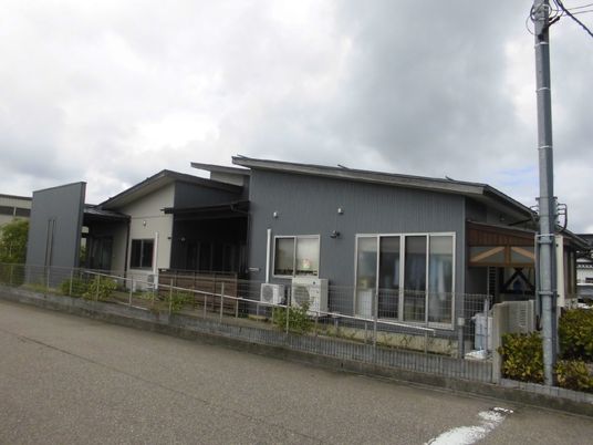 グレーを基調としたすっきりとした外観。平屋建てで建物周辺には緑がある。