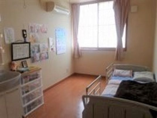 家具や写真などの愛用品に囲まれた居室。ベッドには柵が取り付けられている。