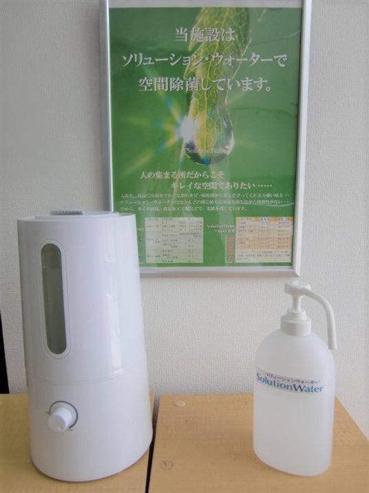 除菌水のポスターの前に置かれた専用の機械とプッシュ式の専用ボトル。