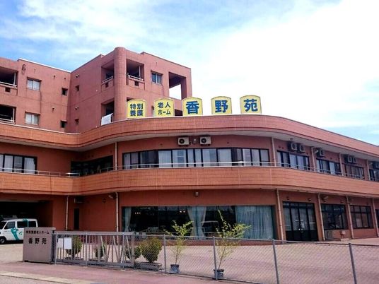 4階建ての建物はブラウン系で広い駐車場やベランダもあり、玄関には住宅名が書かれている。