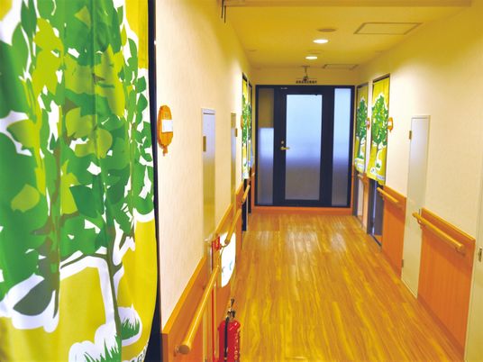 木の絵が描かれている暖簾と施設の廊下の様子。壁には手すりが用意されている