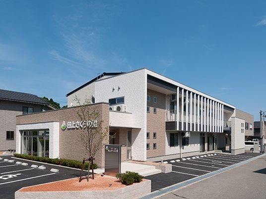 青空の下に建っている２階建てのモダンな建物。駐車場スペースがあるのが分かる