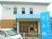 白とベージュの2階建ての建物にはライトブルーの屋根が付いた玄関があり、玄関の前にはブルーの看板も建っている。