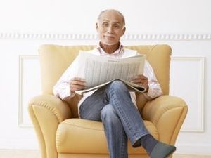 一人用のソファに座ってこちらを向いて微笑む男性。リラックスしている様子