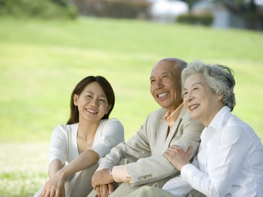屋外の芝生の上に座って楽しそうに話をしている高齢夫婦と女性の姿