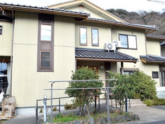 一般の住宅を大きくしたような雰囲気のベージュの外壁の2階建ての建物。洗濯物干し場や木が植えられたスペースがある。