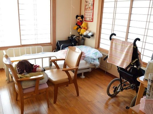 寝具付きのベッドが置かれたフローリングの部屋にはぬいぐるみが飾られ、椅子やシルバーカーも置かれている。