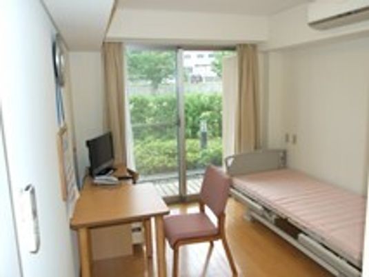 エアコンが付いたフローリングの部屋には介護ベッドやテレビ、デスクセットがある。