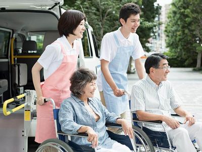 車いすの高齢の男女とエプロンを付けた若い男女のスタッフが笑顔で何かを鑑賞している様子。