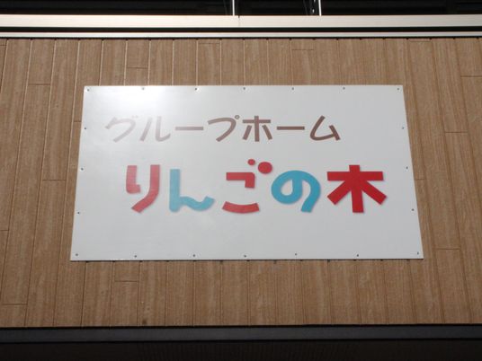 「グループホームりんごの木」と書かれたプレートが貼られたブラウン系の外壁の建物。