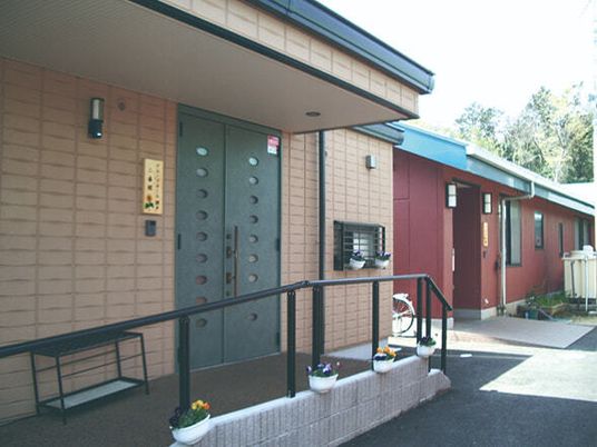 表札がかかったエントランスにはグリーンのドアが付いていて、傘立てがあり、手すり付きの階段もある。