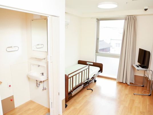 呼び出しボタン付きのトイレが設置されたフローリングの部屋には大きな窓があり、テレビや介護ベッドもある。