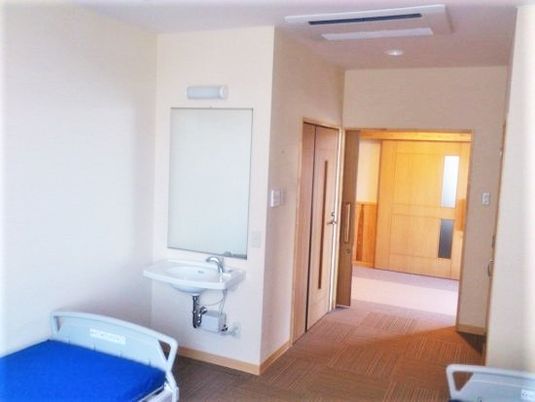 介護仕様のベッドと洗面台、奥のほうにトイレが置いてある個室仕様の部屋の様子
