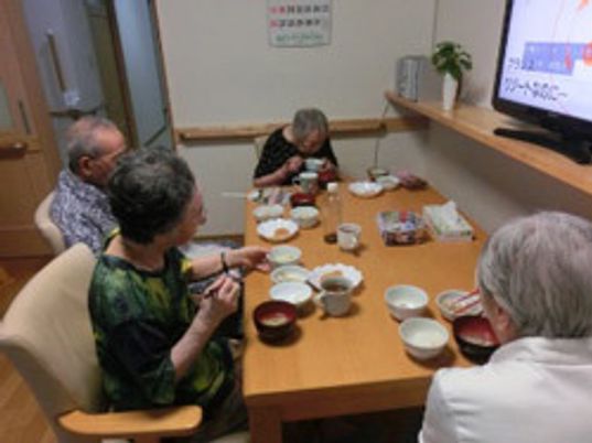 少人数で食卓を囲み、テレビを見ながら食事をしている入居者4名。