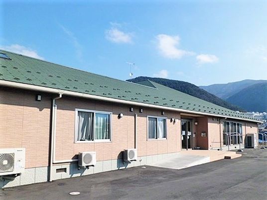 平屋建ての建物。緑の三角屋根が付き玄関にはスロープも設置され、駐車場も付いている。
