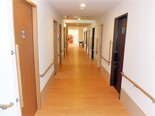 まっすぐな廊下の突き当りには共有スペースがあり、廊下の両サイドには手すりと居室がある。
