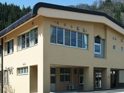 ベージュの外壁の２階建ての建物は日当たり良好で、周りには自然あふれる風景が広がっている。