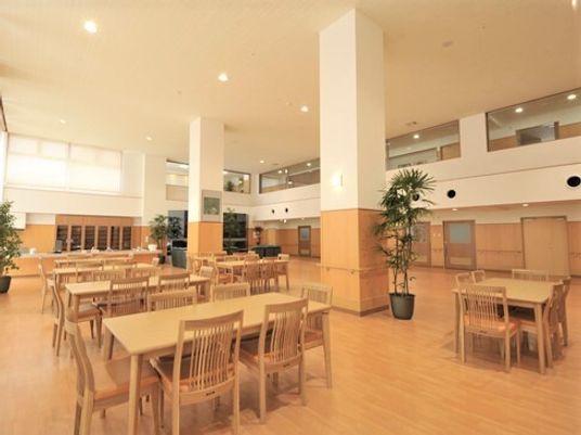 木製のテーブルと椅子が置いてある施設内のリビングスペース。天井が高い様子