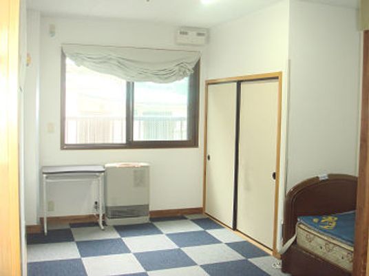 大きな窓から陽の光が降り注ぐ明るい居室。ベッドやヒーター名が置かれた広い部屋。
