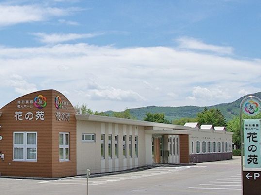 青空の下に建っている平屋。「花の苑」という看板が見える。