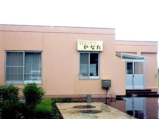 ブラウン系の建物の周りには緑が植えられ、外壁にはホーム名が書かれている。