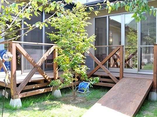 ウッドデッキのテラスがあり、テラスから庭へはスロープが続き、草木も植えられている。