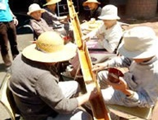 帽子をかぶり椀をもって椅子に座り、そうめん流しを楽しんでいる入居者。