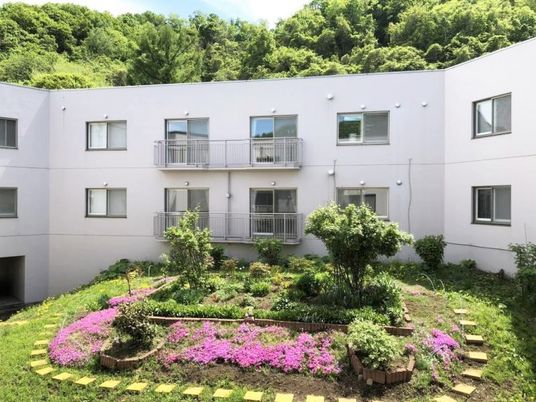 紫の花や木が植えられた中庭があり、その後ろには2階建ての建物が建っている。